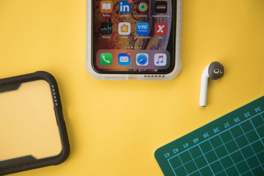 iPhone on yellow table with phone case on left and wireless earbud on right.