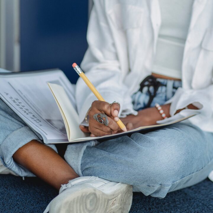 A person sitting and taking notes in a notebook with a pencil.